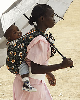 Young woman dressed in pink carries a baby on her back and a silver umbrella in her hand. Nairobi, Kenya