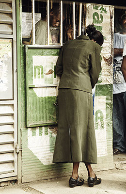 Woman hides her face while speaking to a man through a window, dressed in green