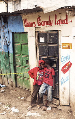Two boys in red whisper in front of a "Candy Land" structure in Nairobi, Kenya